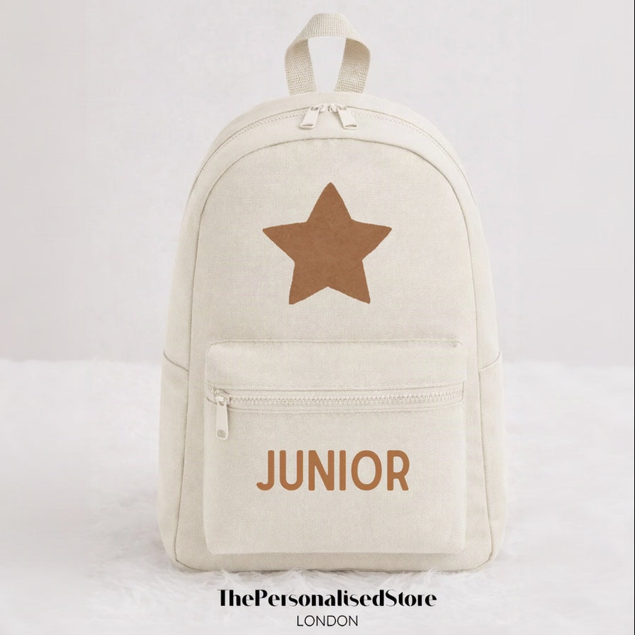 An off-white canvas backpack with a brown star on the front and the word 'JUNIOR' printed in brown below the zipper, shown against a light gray background.