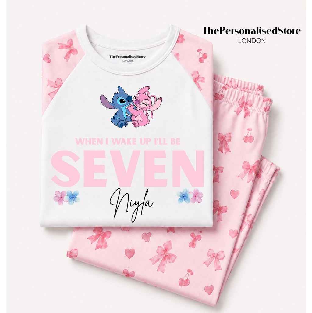 A folded children's pajama set on a light beige background, featuring a white raglan top with pink sleeves and a cartoon character graphic, paired with matching pink pajama pants printed with bows and hearts. The text 'ThePersonalisedStore LONDON' is visible in the top right.